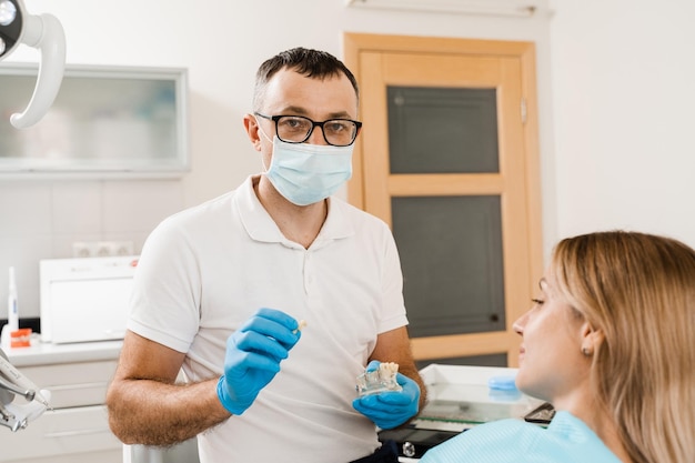 Dental prosthetics and implants Doctor dentist shows artificial plastic jaw with dental implants Dental prosthetics consultation with dentist for patient woman in dentistry