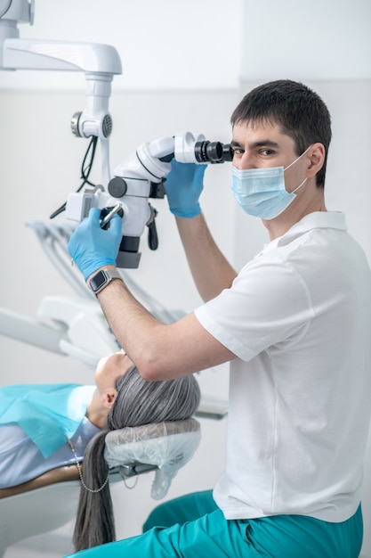 Dental surgery. Male dentist working using optical medical instrument while doing a dental restoration