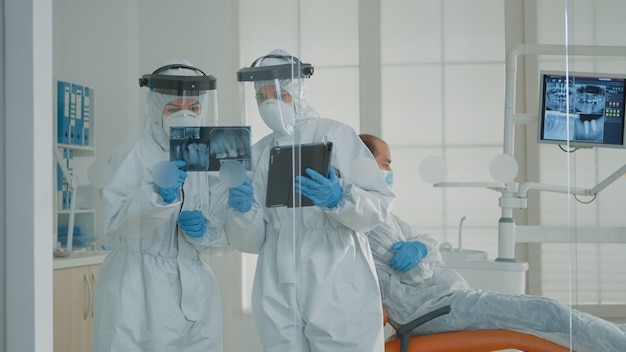 Dentist and assistant examining x ray and tablet at oral clinic