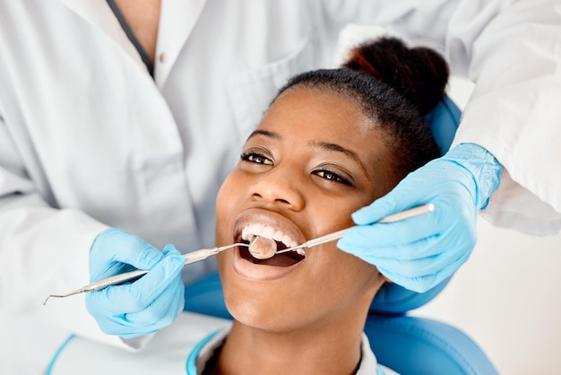 Dentist black woman and patient at a clinic with medical and healthcare for teeth cleaning Mirror orthodontist and African female person with wellness and dental work tool in mouth with care