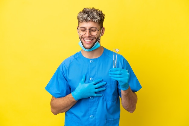 Dentist caucasian man holding tools isolated on yellow background smiling a lot