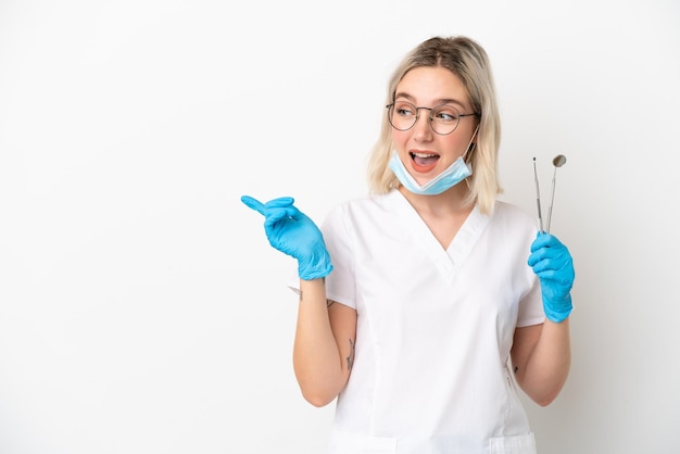 Dentist caucasian woman holding tools isolated on white background pointing finger to the side and presenting a product