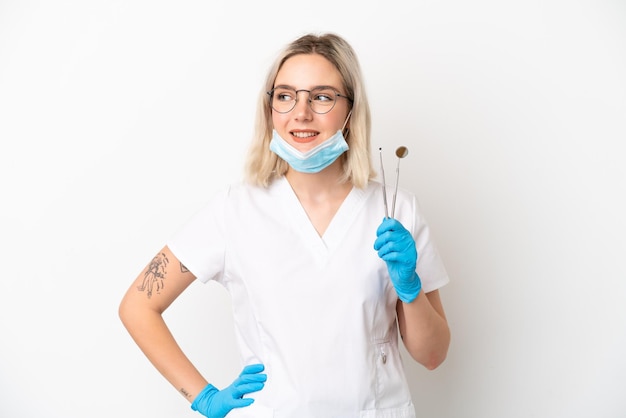 Dentist caucasian woman holding tools isolated on white background posing with arms at hip and smiling