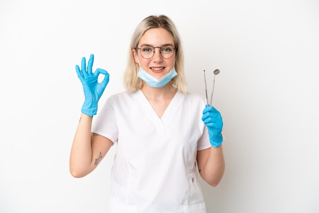 Dentist caucasian woman holding tools isolated on white background showing ok sign with fingers