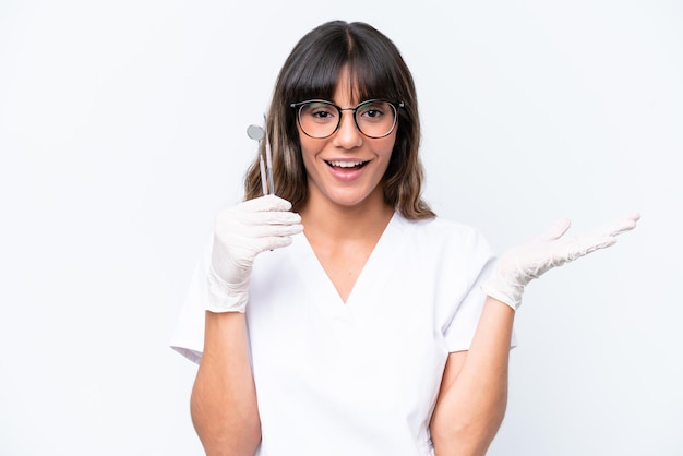 Dentist caucasian woman holding tools isolated on white background with shocked facial expression