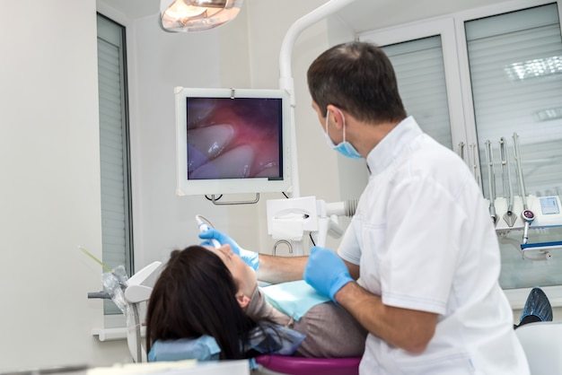 Dentist checking patient's teeth with camera, looking on screen