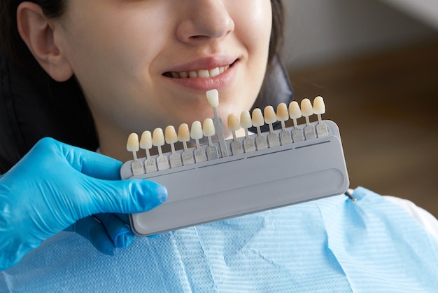 Dentist choosing color of tooth enamel for patient Dentist applying sample from tooth enamel scale to caucasian female teeth