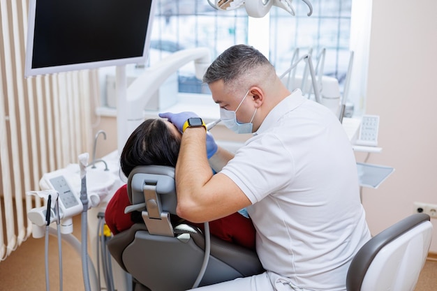 The dentist doctor looks at the patient's teeth and holds dental instruments near the mouth The assistant helps the doctor They wear white uniforms with masks and gloves Dentist Dental office