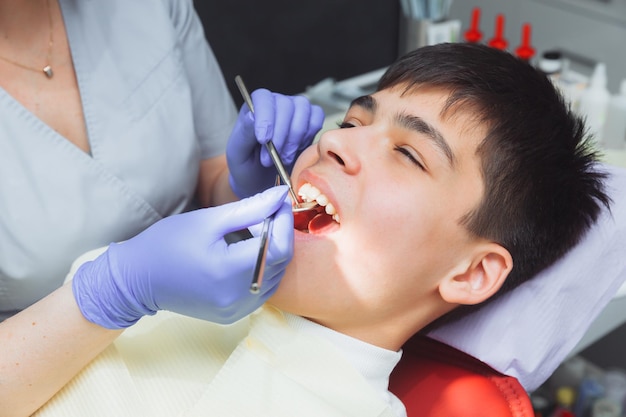 The dentist examines the teeth of a boy of 13 years old in the clinic pediatric dentistry