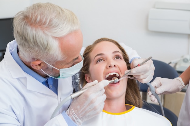 Dentist examining a patients teeth in the dentists chair with assistant