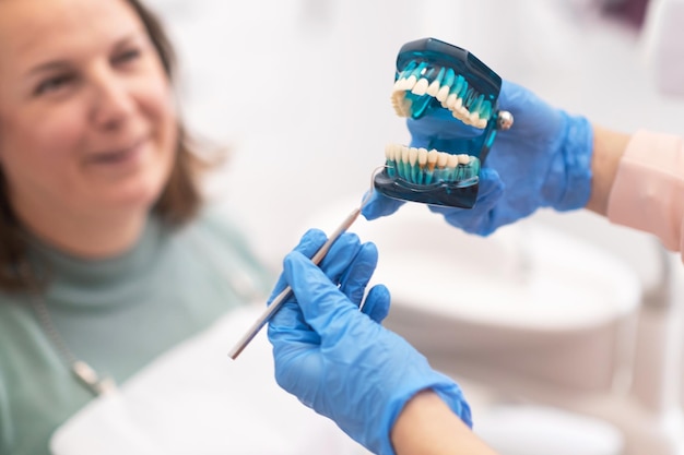 Dentist explaining treatment plan to woman patient holding jaw dental model teeth problems close up