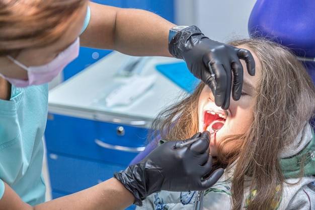 Dentist making teeth examination procedure for little girl sitting on chair in Dentist office