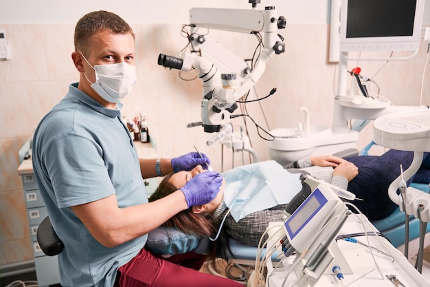 Dentist in medical mask examining patient teeth in dental office