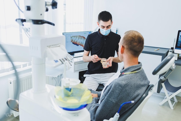 A dentist in a modern dental office tells a patient about dental care A man sits in a dental chair and listens to a dentist