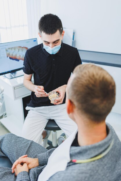 A dentist in a modern dental office tells a patient about dental care A man sits in a dental chair and listens to a dentist