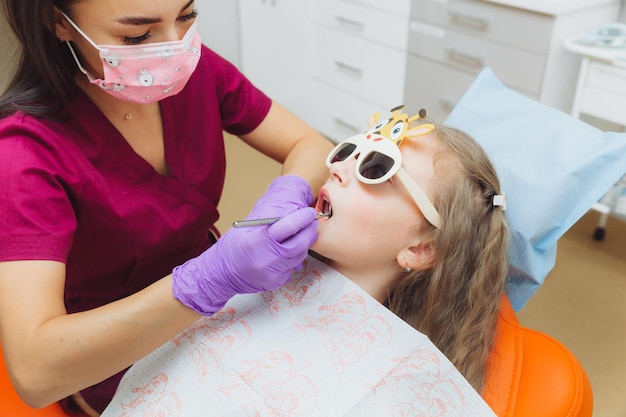 The dentist performs an examination procedure on a cute little girl Little girl sitting in the dentist's office