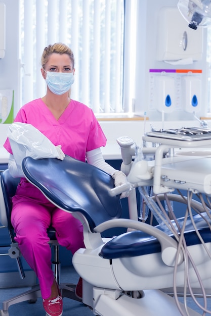 Dentist in pink scrubs looking at camera beside chair