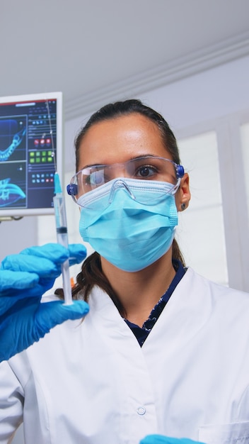 Dentist preparing anesthesia before tooth surgery, holding syringe with serum, pov patient. Doctor and nurse working in modern orthodontic office wearing protection mask and gloves