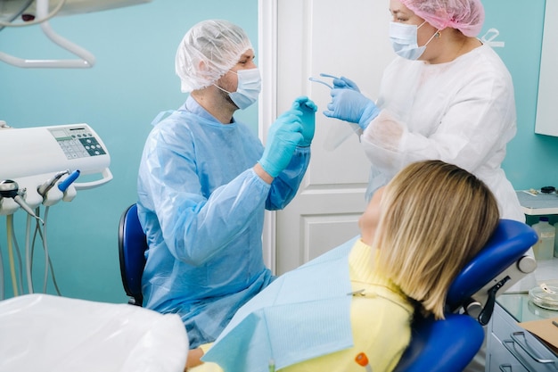 A dentist in a protective mask treats a patient in a dental office with an assistant