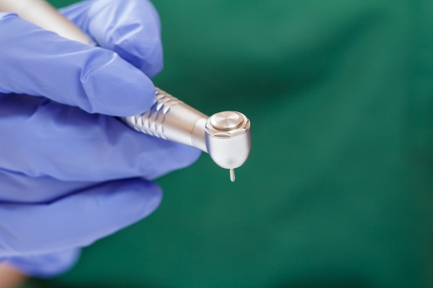 Dentist's hand in a blue latex glove with new high-speed dental handpiece on blurred background. Medical tools concept.