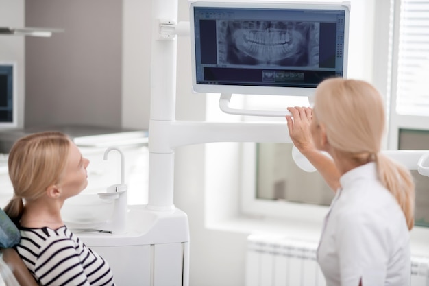 Dentist showing the interested patient her jaw x-ray on the big screen in her office