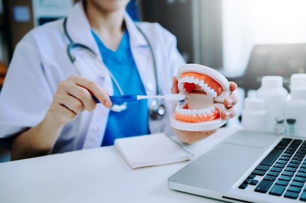 Photo dentist sitting at table with jaw samples tooth model and working with tablet and laptop in dental office professional dental clinic