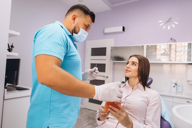 The dentist smiles and shows the girl a model with teeth talks about implantation and caries