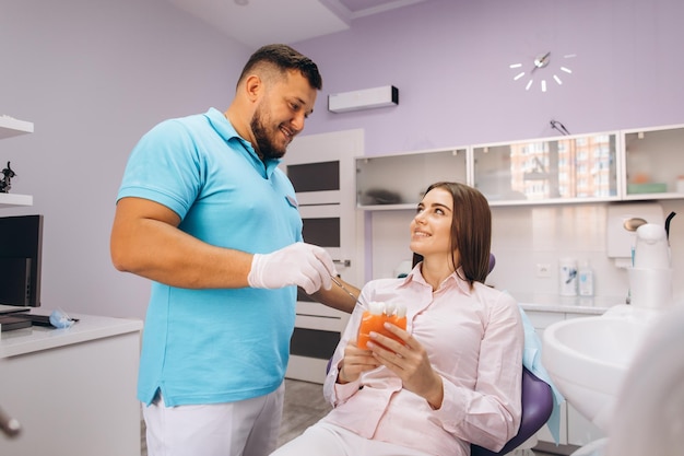 The dentist smiles and shows the girl a model with teeth talks about implantation and caries