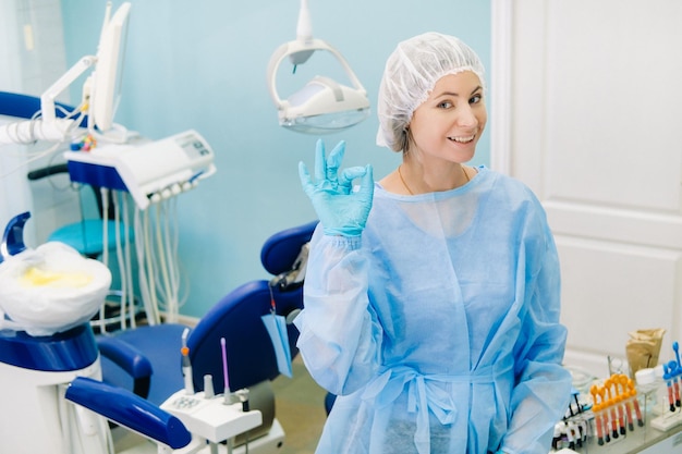 The dentist stands in his office and shows the OK sign