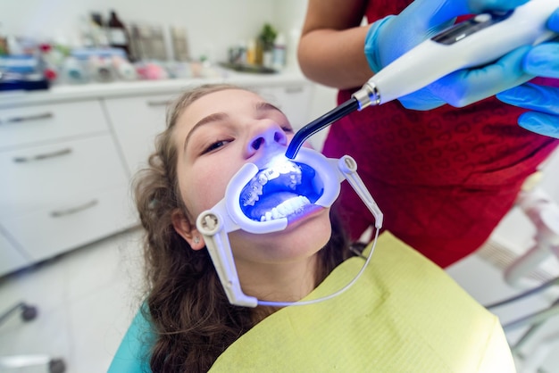 The dentist uses an ultraviolet lamp while fitting the girl with braces