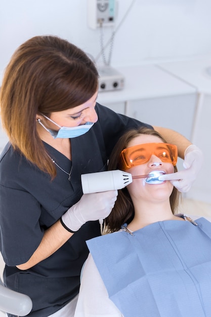 Dentist using whitening laser on female patient