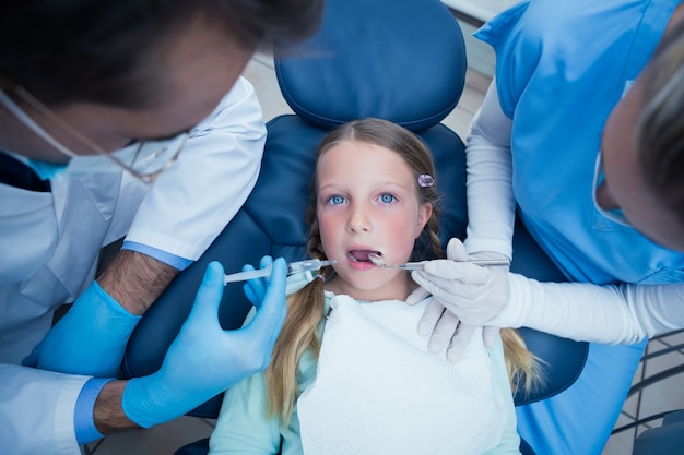 Dentist with assistant examining girls teeth