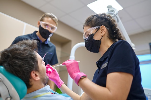 Dentist with assistant treating patient teeth. Man having tooth examination at dental consultation