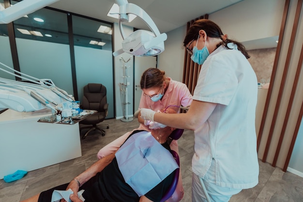 A dentist with the help of a colleague performs an operation on the jaw of an elderly patient in a modern dental clinic. High quality photo