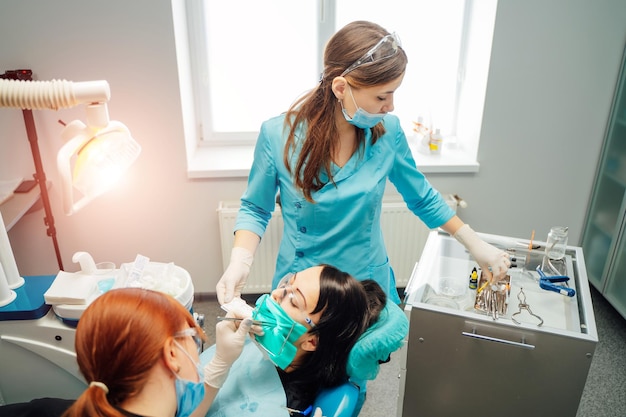 Dentist woman and her assistant in medical clothes treating patient's teeth in a stomatological centre Dental cure Toothcare concept