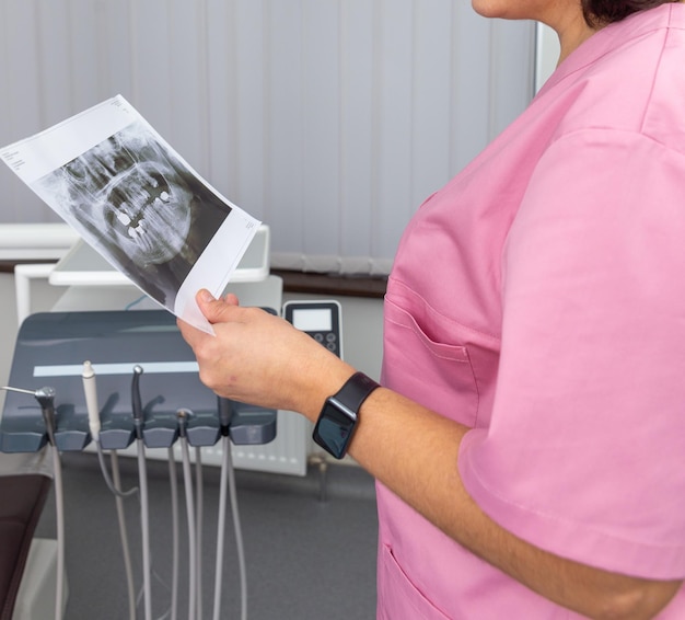 Dentist woman in pink uniform looking at roentgen of human jaw