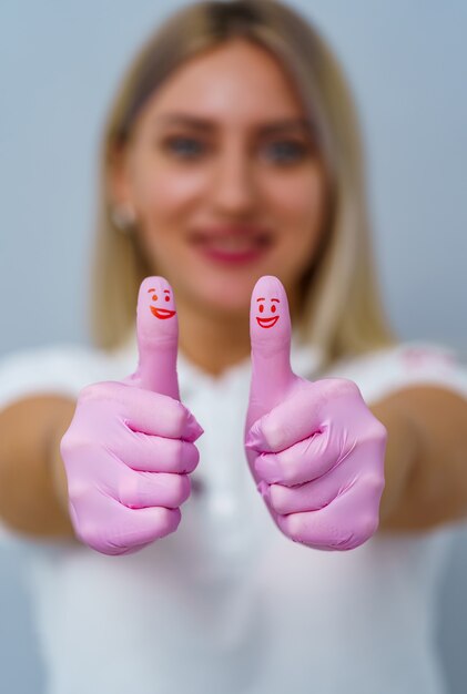 Dentist woman with pink gloves. Showing cool sign. Red smiles on thumbs.