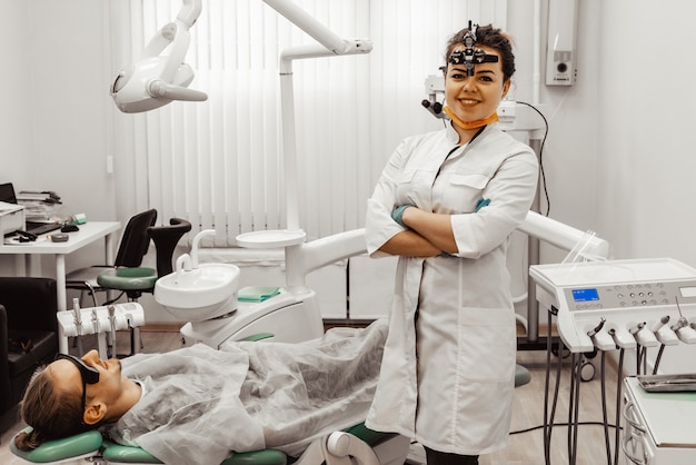 Dentist young woman treats a patient a man. The doctor uses disposable gloves, a mask and a hat