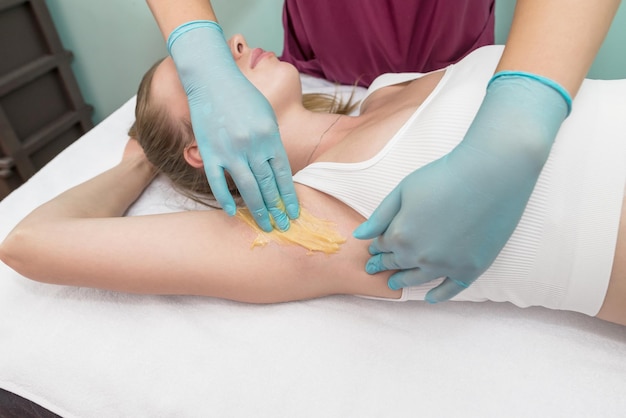 Depilation and epilation of the female armpit with liquid sugar paste The beautician's hand applies wax paste to the armpit The concept of smooth armpits