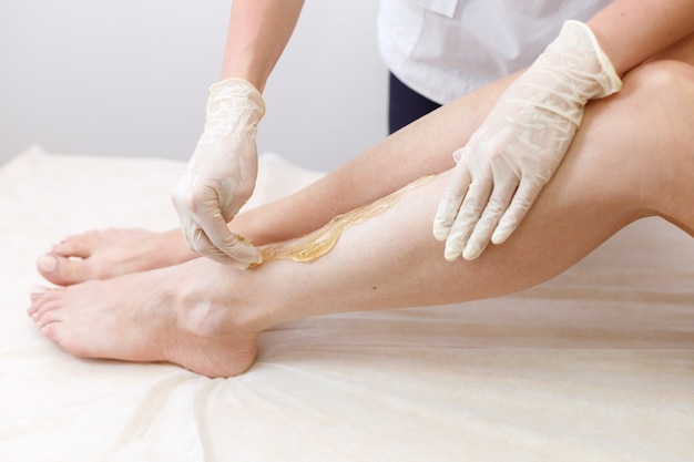 Depilation master applies sugaring paste legs