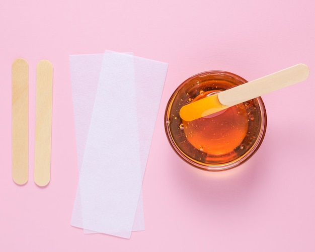 Depilatory sugar paste with a wooden spatula and depilatory strips on a pink background Epilation