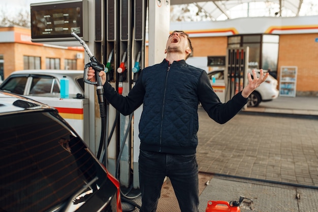 Depressed man cries on gas station, high price on fuel. Petrol fueling, gasoline or diesel refuel service, petroleum refueling