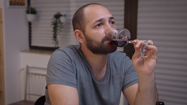 Depressed man drinking alone in the kitchen. Unhappy person suffering of migraine, depression, disease and anxiety feeling exhausted with dizziness symptoms having alcoholism problems.