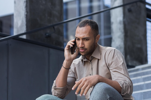 Depressed man sitting on stairs of office building frustrated talking on phone upset and fired