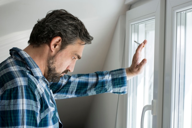 Depressed man with cigarette standing besides window