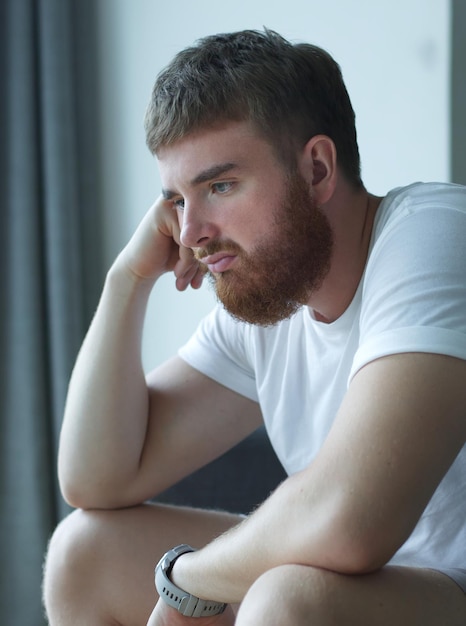 Depressed unhappy middleaged sad man sitting on couch in living room leaning on his hands having