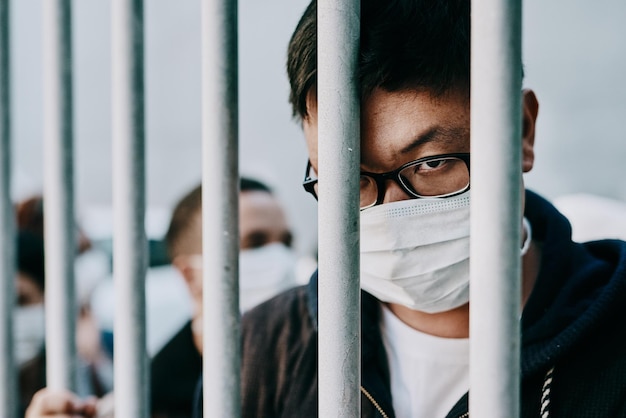 Depressed upset or sad covid patient stuck in the city feeling like a prisoner wearing a medical face mask Foreign asian man in a crowd during pandemic holding area following city healthcare rules