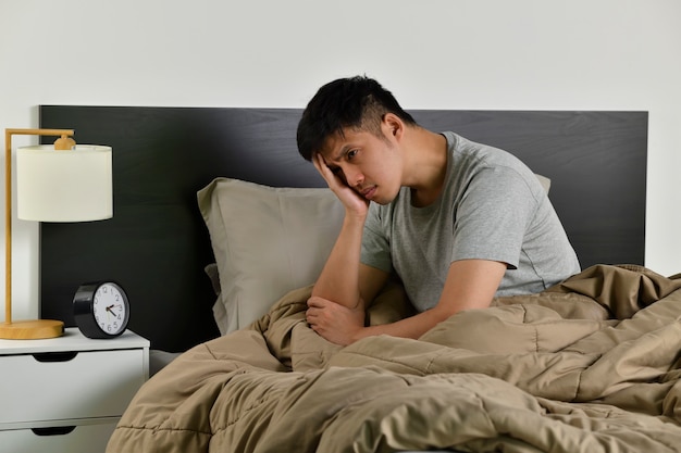 Depressed young Asian man sitting in bed cannot sleep from insomnia