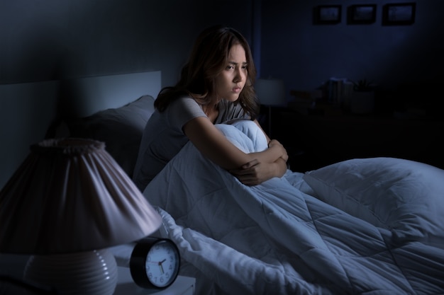 Depressed young Asian woman sitting in bed cannot sleep from insomnia

