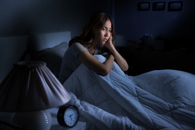 Depressed young Asian woman sitting in bed cannot sleep from insomnia

